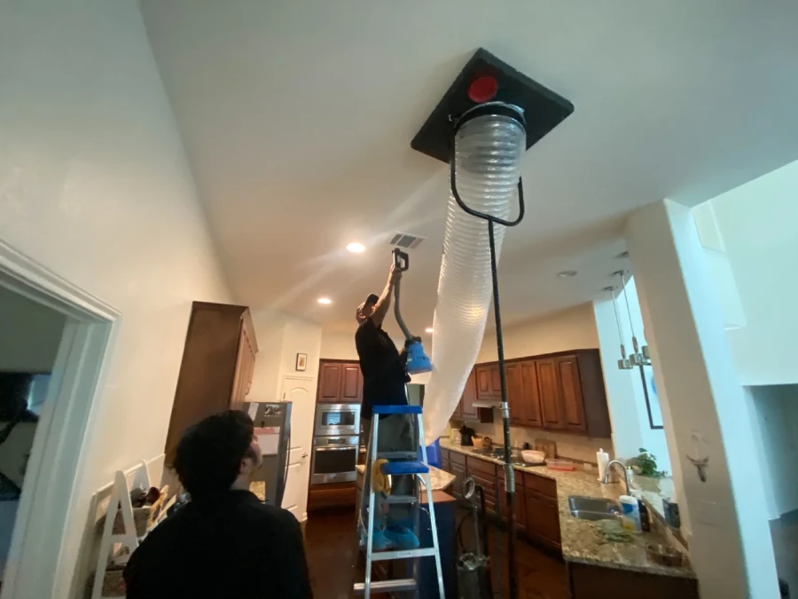 Negative air machine attached to the ceiling and a technician using vacuum brush to clean the ducts.